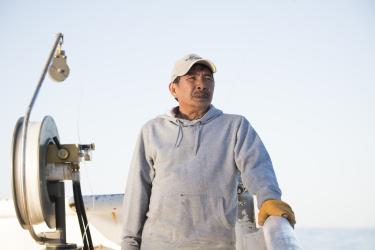 Man stands along the railing of a fishing vessel, next to a rig