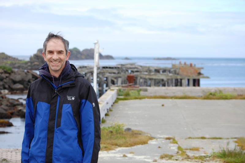 Man in blue and black coat with coast and water in background